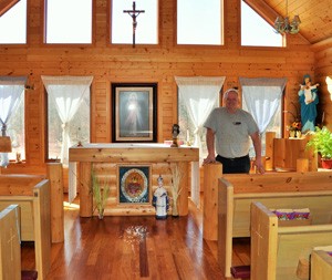 Ed Cycenas stands in the consecrated chapel at Monte Christo in Siren. Cycenas built the altar, chair and other log pieces and installed wood paneling throughout the lodge. He made the stained glass Sacred Heart in the altar from a broken windshield. (Catholic Herald photo by Anita Draper)